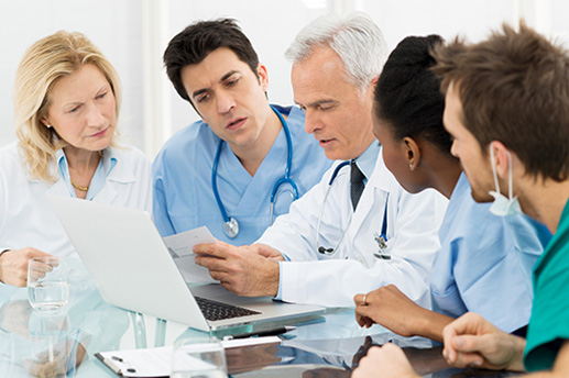 A group of doctors are gathered around a laptop.